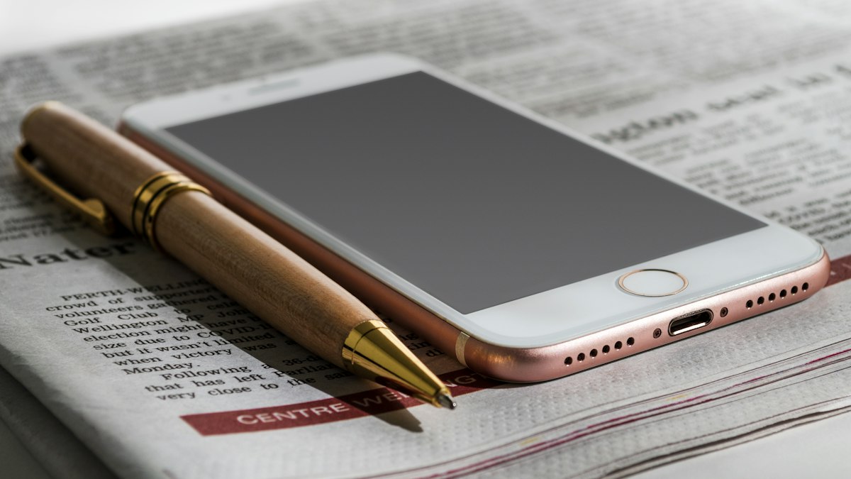 A smartphone and a wooden ballpoint pen lying on a folded printed newspaper