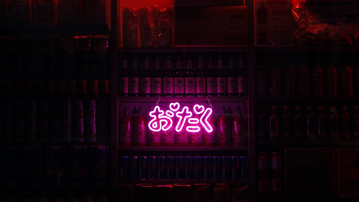 A pink neon sign in Japanese hiragana glowing in a dark shop